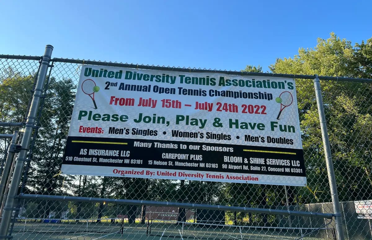 A banner for United Diversity Tennis Association's 2nd Annual Open Tennis Championship, held July 15–24, 2022, hangs on the court fence.